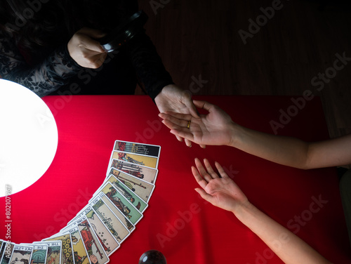 An overhead view of a tarot card reading in progress with a palm reading and cards laid out on a red tablecloth