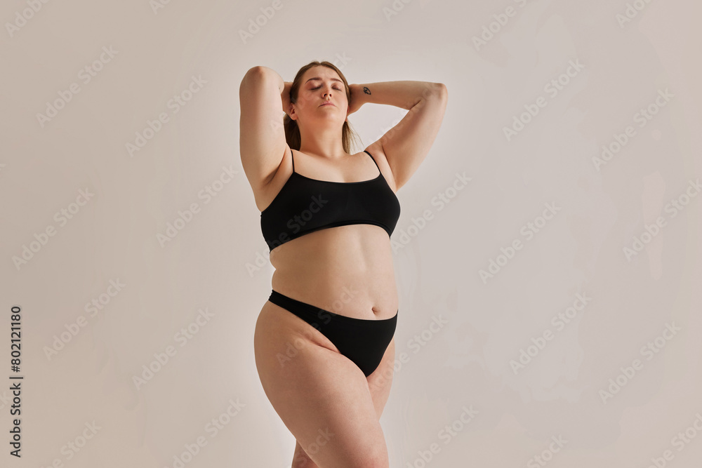 Serene expression of self-love. Young elegant girl with plus size body shape posing in underwear against grey studio background. Concept of natural beauty, body positivity, care, acceptance Serene expression of self-love. Young elegant girl with plus size body shape posing in underwear against grey studio background. Concept of natural beauty, body positivity, care, acceptance