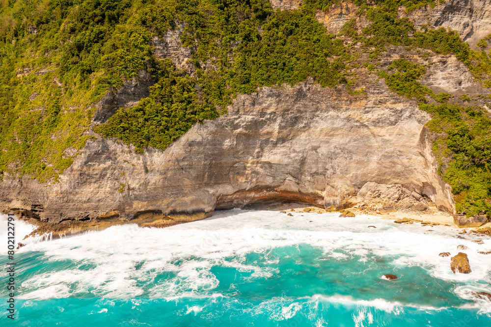 High rocks with green tropical vegetation, foamy sea water. Drone type. Bali, Klungkung, Indonesia.