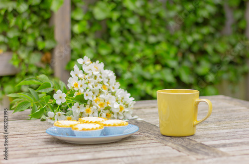 yellow cup and cupcakes on the table in garden on the background of white flowers