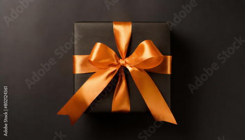 Top view photo of black giftbox with orange satin ribbon bow on isolated black background with copyspace 