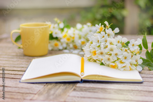 open notebook , yellow cup and white flowers on wooden table in garden