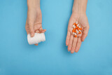 Top view of female hands with pills and bottle on blue background.