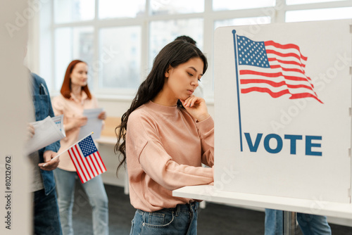 Pensive young woman, Asian voter waiting in line standing in polling booth voting at polling station photo