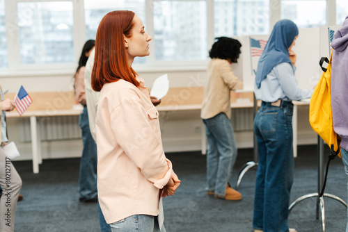 Attractive woman with red hair standing at polling station waiting in line to voting in US election