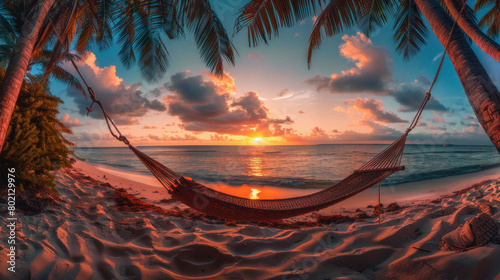 A hammock is hanging over the ocean, with the sun setting in the background
