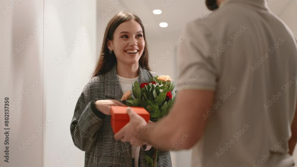 A smiling young woman receiving a bouquet and a gift box from a delivery service. Expresses happiness and surprise. A smiling young woman receiving a bouquet and a gift box from a delivery service. Expresses happiness and surprise.