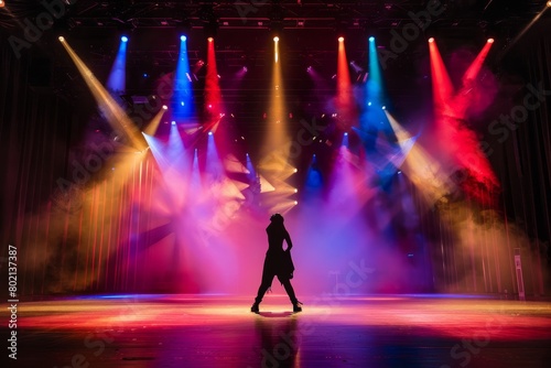 A person stands in front of an empty stage illuminated by vibrant colorful lights