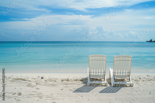 Two white beach chairs are sitting on the sand  facing the ocean