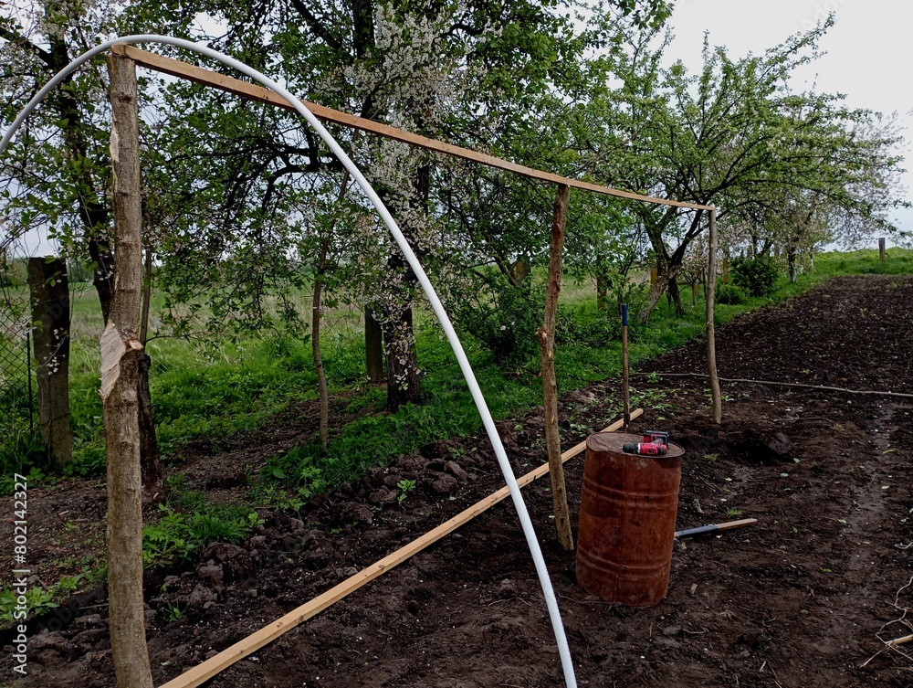 Fototapeta premium A wooden frame that supports pipes over which polyethylene film will be stretched to create a greenhouse in your own garden with your own hands from materials at hand. Frame of a greenhouse for growin