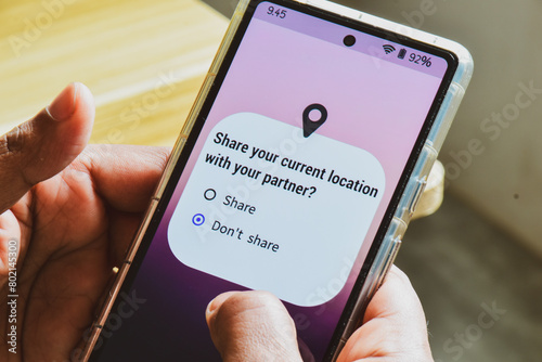 Mobile phone screen displaying the message Share your current location with your partner. Person decision not to allow it. Couple relationship trust issues concept.