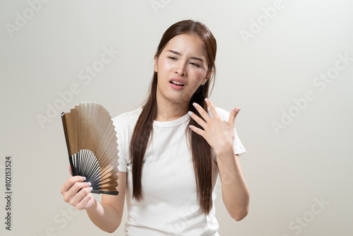 Suffering summer heat wave stroke, hot weather, tired asian young woman sweaty and thirsty, refreshing with hand in blowing, wave fan to ventilation when temperature high, isolated on background.