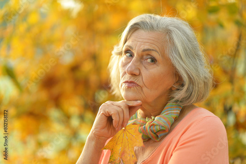 Portrait of beautiful sad senior woman on blurred autumn background