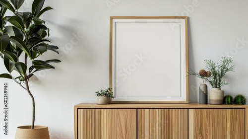 A white framed picture sits on a wooden cabinet. The cabinet is filled with various potted plants, including a large fern and a smaller one. The room has a clean and minimalist feel