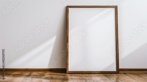 A wooden framed white picture is sitting on a wooden floor. The frame is empty, and the picture is not visible