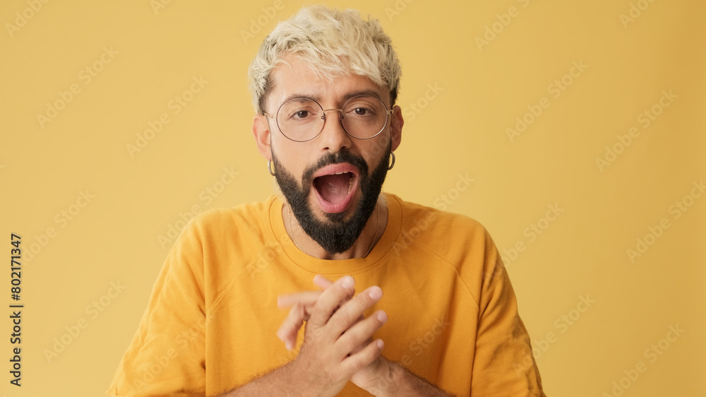 Close up, guy with glasses, dressed in yellow T-shirt, looking at camera with big eyes, says wow, isolated on yellow background in studio Close up, guy with glasses, dressed in yellow T-shirt, looking at camera with big eyes, says wow, isolated on yellow background in studio