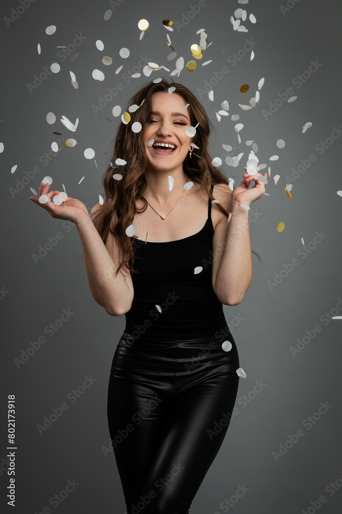 Studio portrait of young beautiful happy woman in black outfit against gray background.