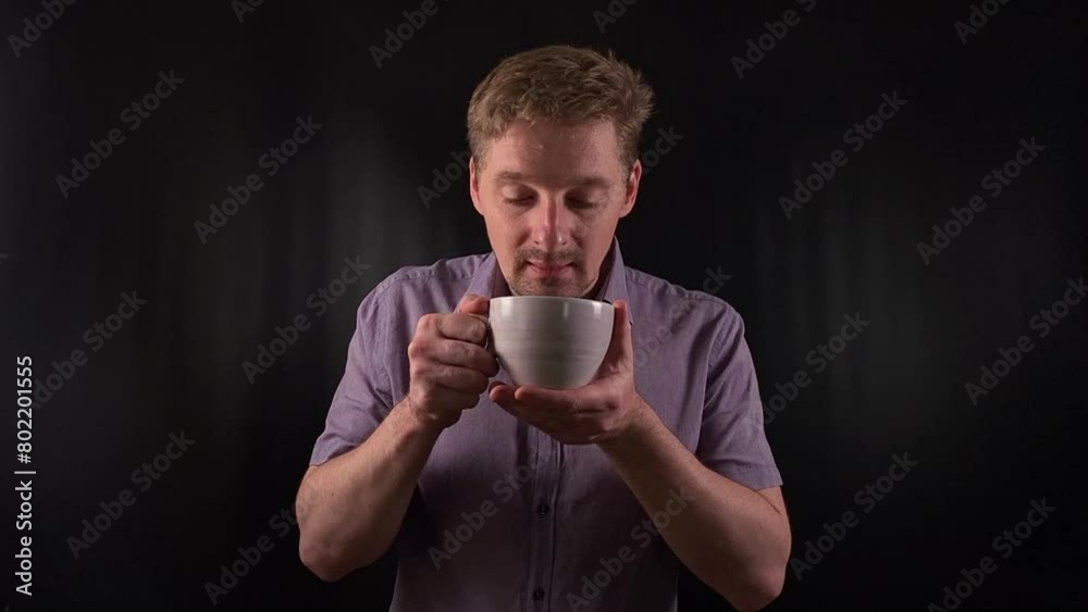 Stylish portrait of a trendy young man sipping a hot drink. Dressed in a vibrant purple shirt he exudes an effortlessly cool demeanor on the black backdrop. Lifestyle, beverage or fashion