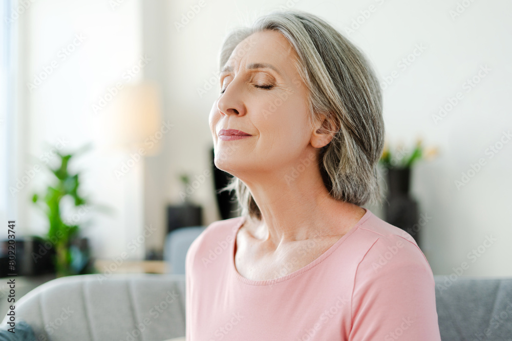 Smiling active senior woman sitting with closed eyes on comfortable sofa relaxing at home Smiling active senior woman sitting with closed eyes on comfortable sofa relaxing at home