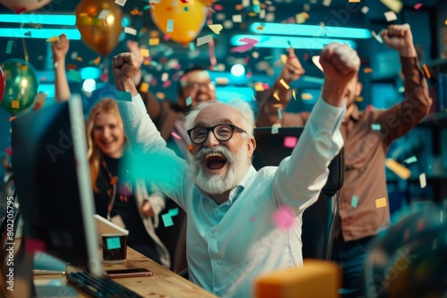 Cheerful senior businessman is celebrating success in the office. He is raising his hands up and looking at the camera.