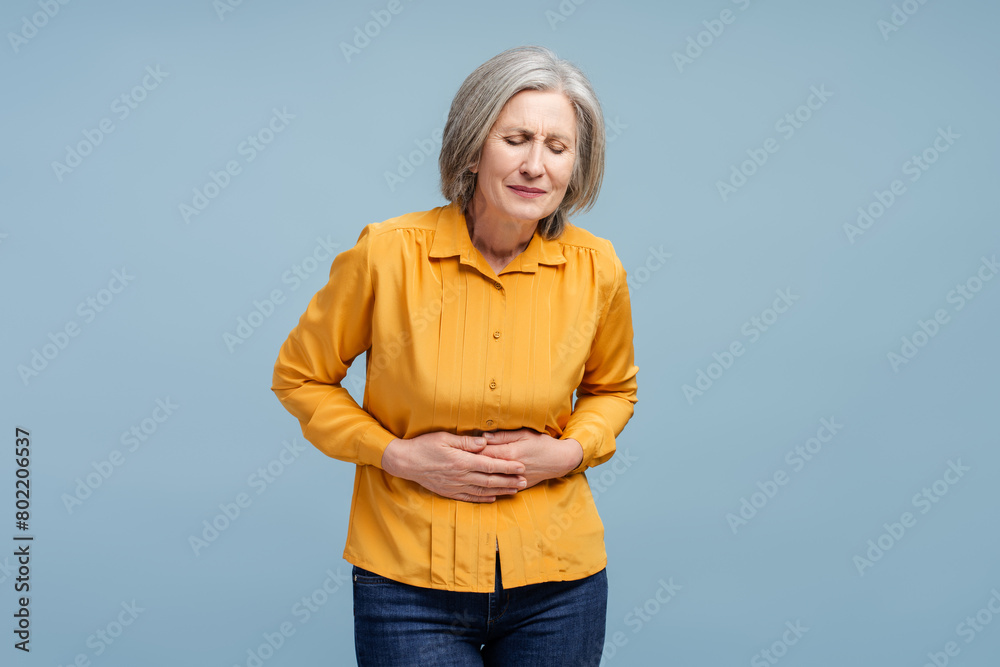 Senior woman holding belly having stomach ache isolated on blue background Senior woman holding belly having stomach ache isolated on blue background