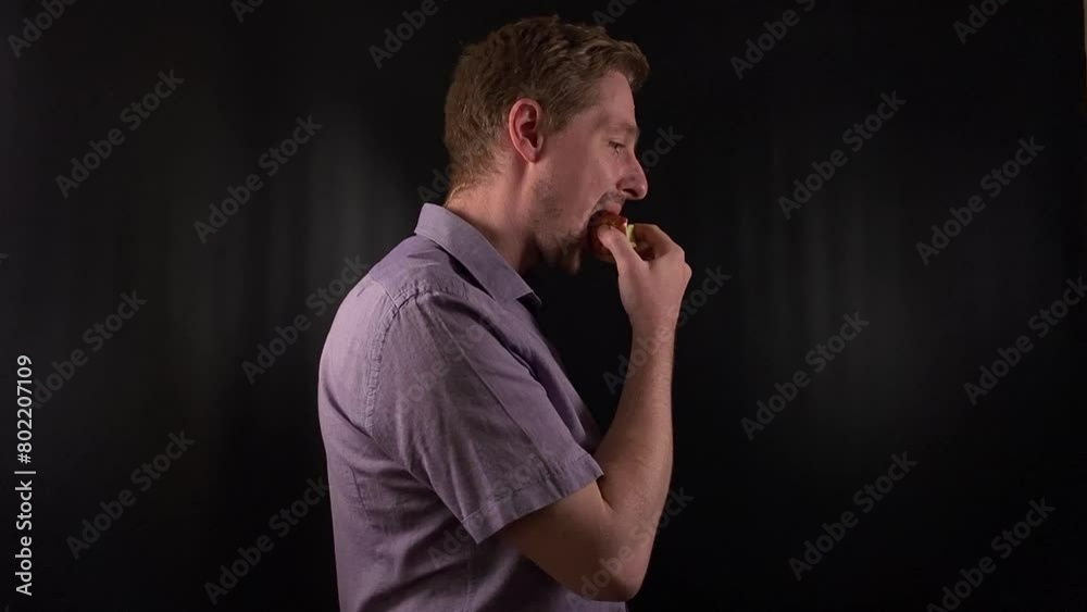 Captivating portrait of a stylish young man with stubble, donning a vibrant purple shirt on a sleek black backdrop, takes bites of meal, exuding an effortless cool vibe. Lifestyle, fashion or culinary Captivating portrait of a stylish young man with stubble, donning a vibrant purple shirt on a sleek black backdrop, takes bites of meal, exuding an effortless cool vibe. Lifestyle, fashion or culinary
