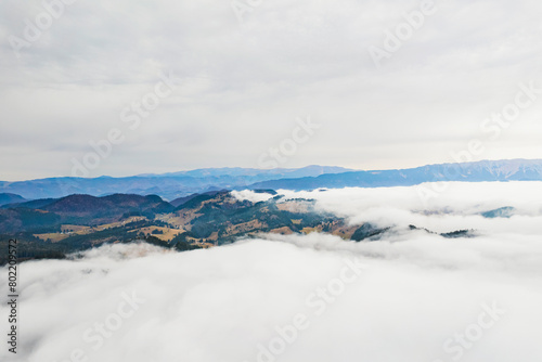 From a birds eye perspective  a magnificent mountain range emerges above a sea of fluffy white clouds  creating a surreal and breathtaking view