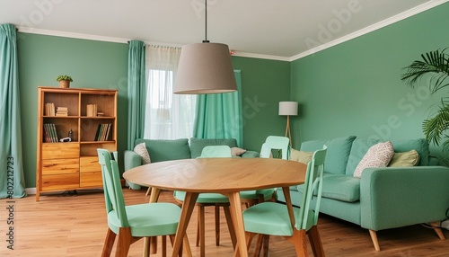 Mint color chairs at round wooden dining table in room with sofa and cabinet near green wall. Scandinavian, mid-century home interior design of modern living room © Louis