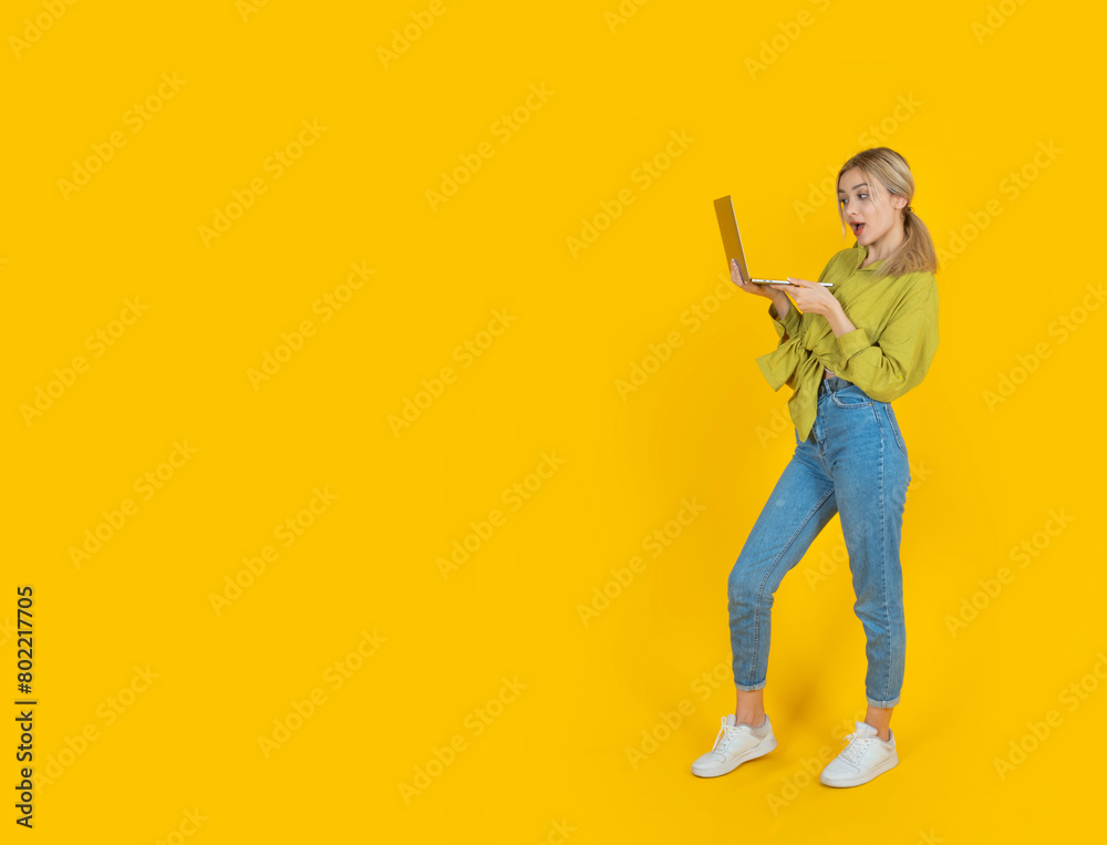 Great online offer, excited caucasian blonde 20s full body length woman holding laptop looking screen on yellow studio background, copy space. Freelance, internet study, student using computer. Great online offer, excited caucasian blonde 20s full body length woman holding laptop looking screen on yellow studio background, copy space. Freelance, internet study, student using computer.