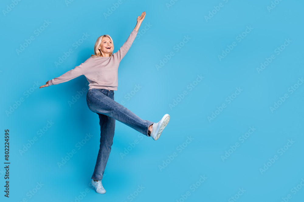 Full body photo of lovely senior lady spread hands flying dancing dressed stylish gray garment isolated on blue color background