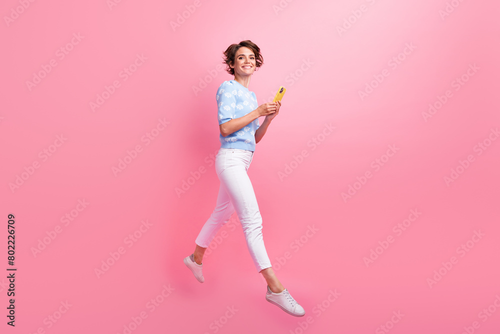 Full length profile portrait of energetic carefree person jump use smart phone empty space isolated on pink color background Full length profile portrait of energetic carefree person jump use smart phone empty space isolated on pink color background
