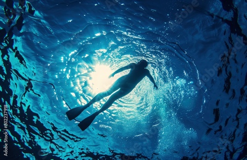 A person swimming underwater, with the sun shining coming on top of water surface. © People