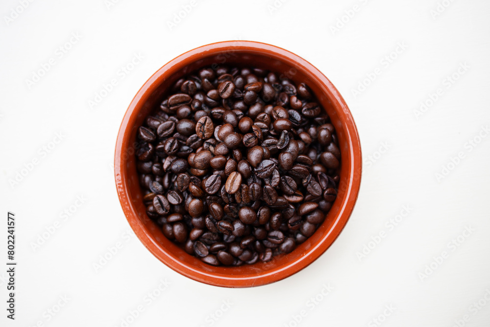 Terracotta ceramic round holder with whole coffee beans against a white wood background Terracotta ceramic round holder with whole coffee beans against a white wood background