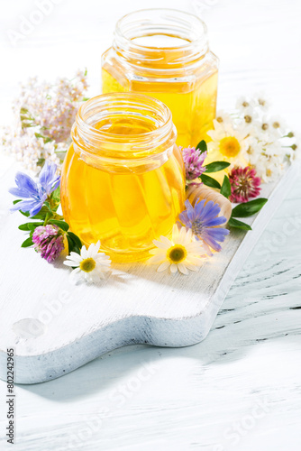 jars with fresh flower honey on white board, vertical top view © cook_inspire