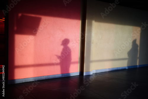 The shadow of a man on the wall, a man watching the departure screen. Silhouettes of people with a reflection on the wall .The shadow of a man on a concrete wall, red in hue. High quality photo