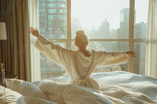 Woman stretching hands in bed after wake up, sun flare . Brunette entering a day happy and relaxed after good night sleep and back view. Concept of a new day and joyful weekend