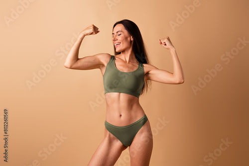 No filter photo of stunning sporty woman showing her muscular arms after gym exercises isolated on beige color background © deagreez