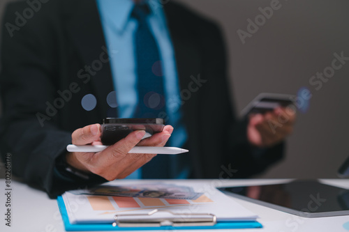 The businessman, holding a smartphone and credit card, seamlessly conducts online shopping and payments from the office, leveraging technology to enhance business transactions.
