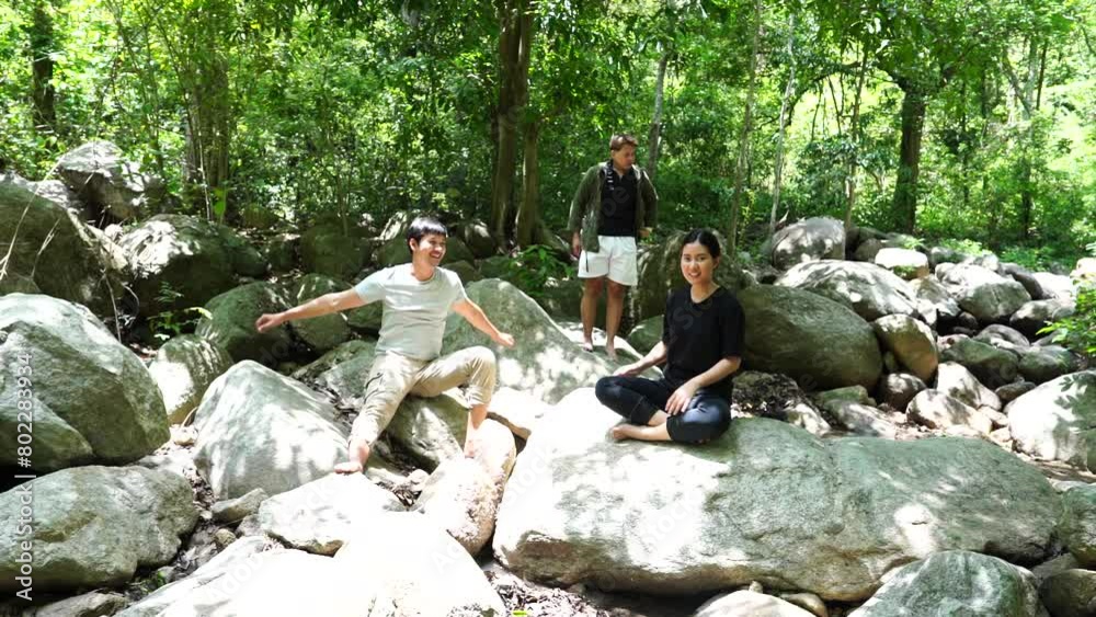Group of three Asian friends, two men and one woman, have a good relationship, hiking rock climbing at the waterfall stream in the forest is happy summer time trip the vacation.Lifestyle concept Group of three Asian friends, two men and one woman, have a good relationship, hiking rock climbing at the waterfall stream in the forest is happy summer time trip the vacation.Lifestyle concept