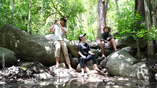Group of three Asian friends, two men and one woman, have a good relationship, hiken rock climbing at the waterfall stream in the forest is happy summer time trip during the vacation.Lifestyle concept
