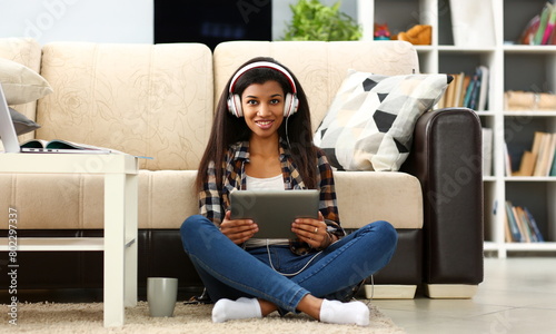 Black ordinary female american teen portrait at home sofa remote education concept. Girl hold tablet in hand music apps teacher checks homework online university library learning foreign languages photo