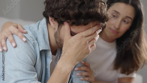 Young caucasian sad man sit on couch at home suffer worried breakdown regret erectile dysfunction loving woman wife hug comforting support empathy crisis impotence potency health
