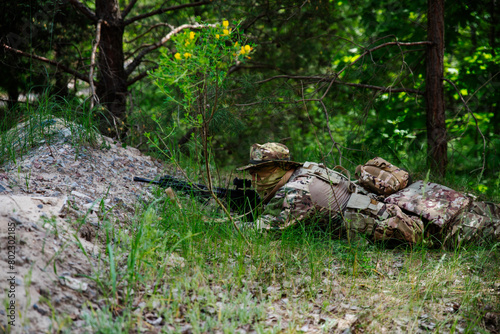 A soldier in camouflage lies in the green grass