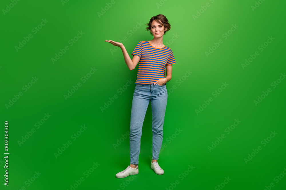 Fototapeta premium Full body portrait of gorgeous positive lady arm palm hold demonstrate empty space isolated on green color background