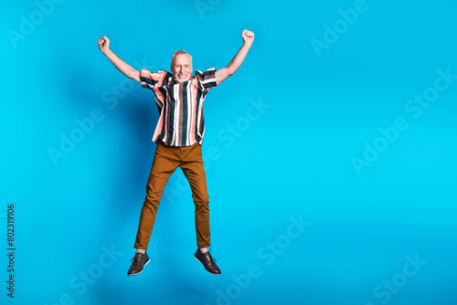 Full length photo of glad cheerful pensioner wear striped stylish clothes raise hand empty space isolated on blue color background