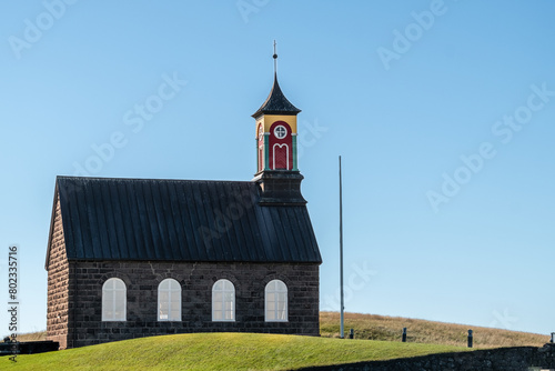 A small church with a red roof and a clock on the front