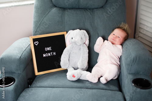 One month old Caucasian baby girl near the plush toy and letter board. Newborn baby monthly picture