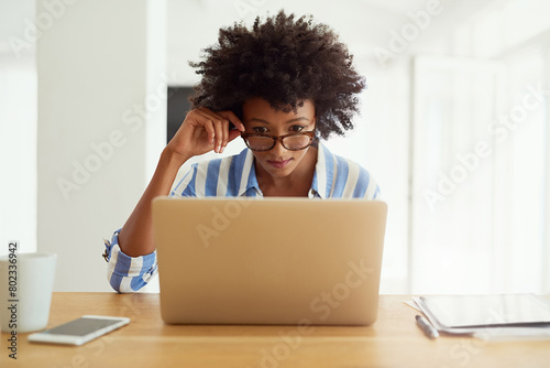 Woman, research and laptop at desk for blog, social media and networking in apartment. African female journalist, glasses and work from home for reading, newspaper article and online magazine photo