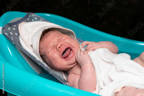 Little newborn baby crying while taking a bath. Caucasian baby crying in a bathtub. Baby care and hygiene 