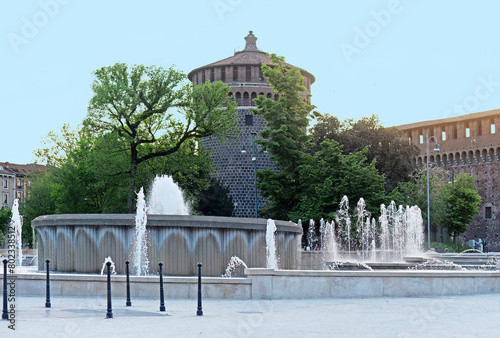 Piazza Castello big round fountain in front of Castello Sforzesco (Sforza Castle) in Milan, Italy, with blue sky
